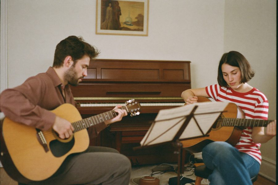 A music teacher giving a guitar lesson to an adult learner in a warm home music room