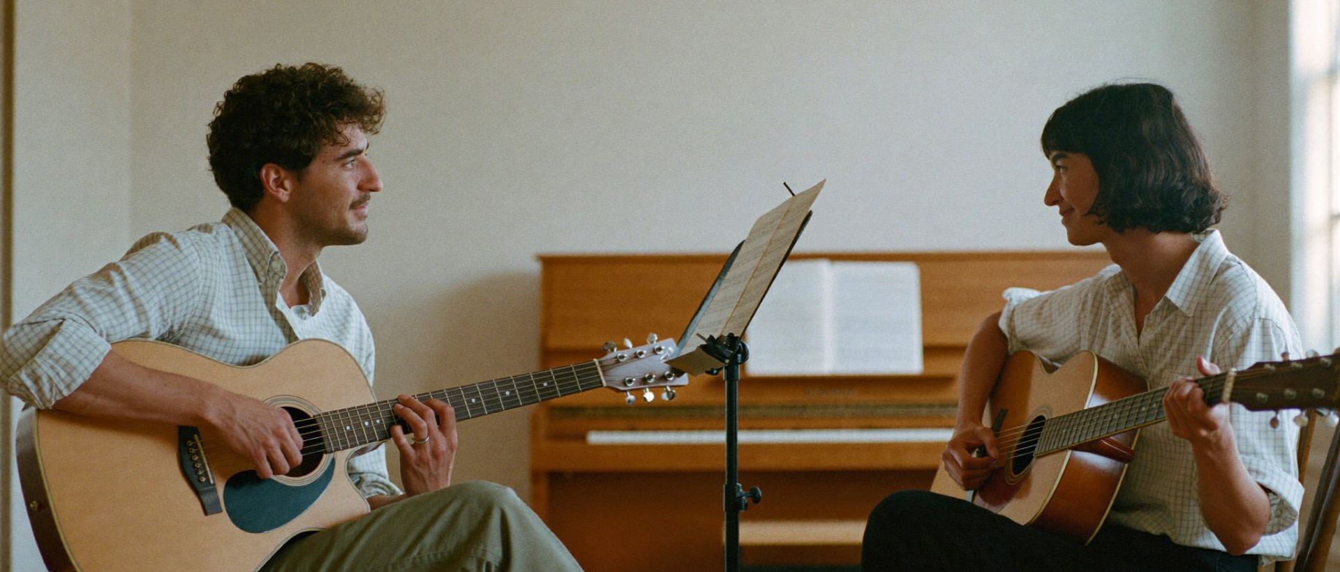 A music teacher giving a guitar lesson to an adult learner in a warm home music room