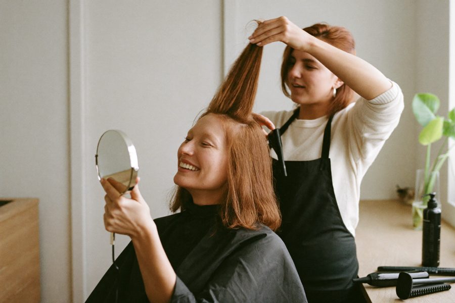 A mobile hairdresser styling a seated client's hair in a bright home kitchen